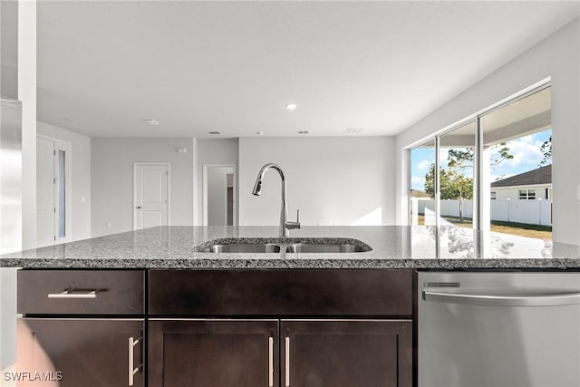 kitchen with stainless steel dishwasher, dark brown cabinets, light stone counters, and sink