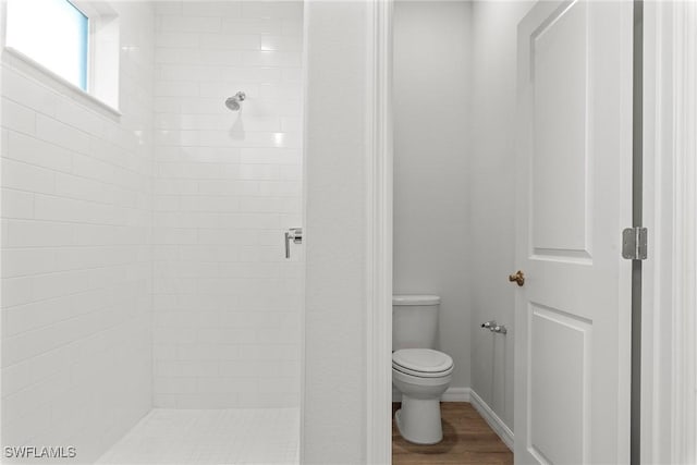 bathroom featuring toilet, a tile shower, and wood-type flooring