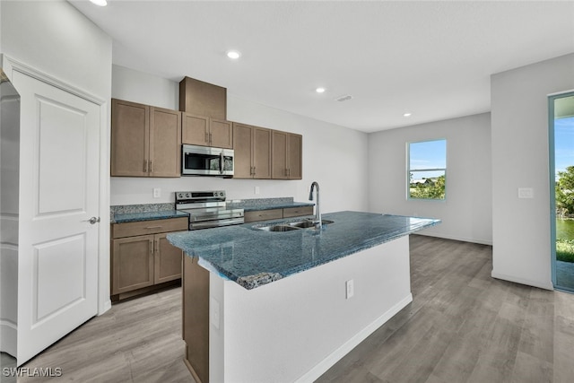 kitchen with sink, stainless steel appliances, a center island with sink, and light hardwood / wood-style floors