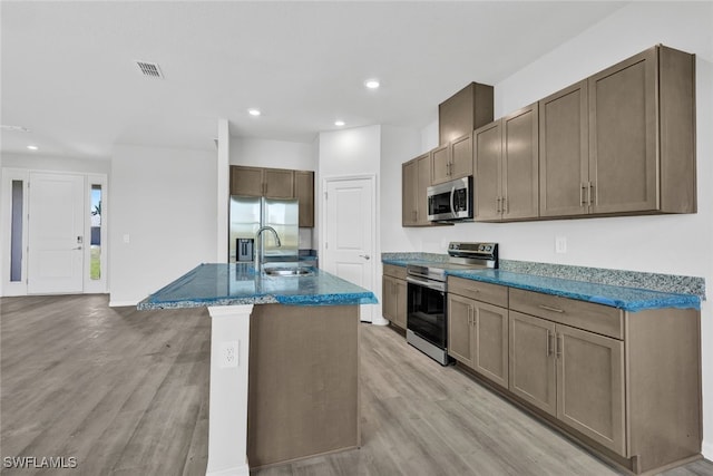 kitchen featuring sink, stainless steel appliances, light hardwood / wood-style flooring, and an island with sink