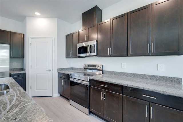 kitchen featuring light hardwood / wood-style floors, light stone counters, dark brown cabinetry, and appliances with stainless steel finishes