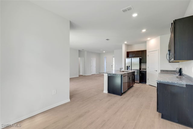 kitchen with light stone countertops, sink, stainless steel appliances, a kitchen island with sink, and light wood-type flooring