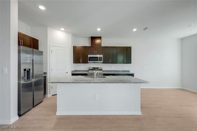 kitchen featuring sink, an island with sink, dark brown cabinets, light stone counters, and stainless steel appliances