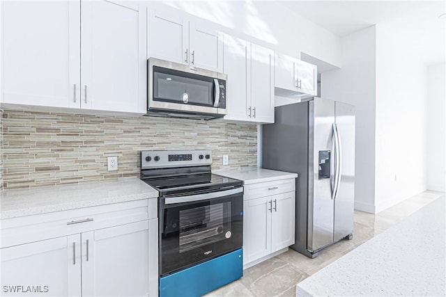 kitchen with tasteful backsplash, appliances with stainless steel finishes, light stone counters, marble finish floor, and white cabinetry