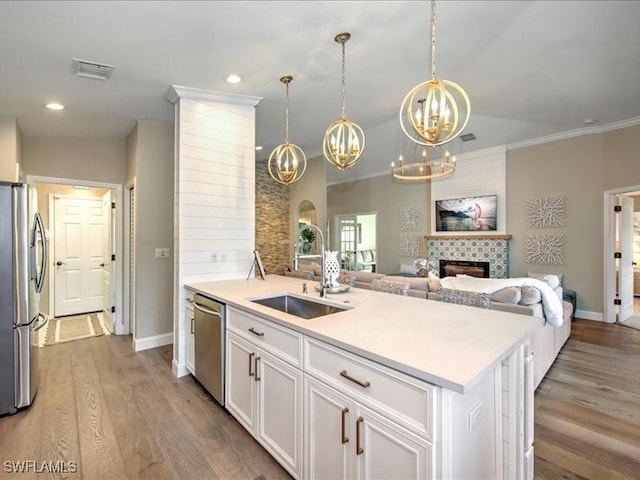 kitchen with white cabinets, sink, an island with sink, appliances with stainless steel finishes, and a tiled fireplace