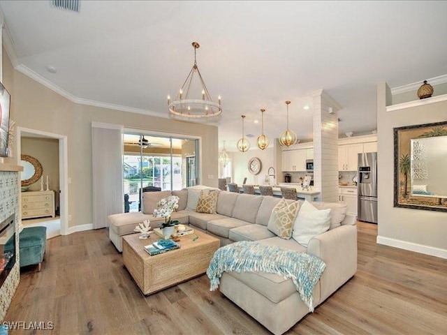 living room featuring ceiling fan with notable chandelier, light wood-type flooring, crown molding, and a tile fireplace