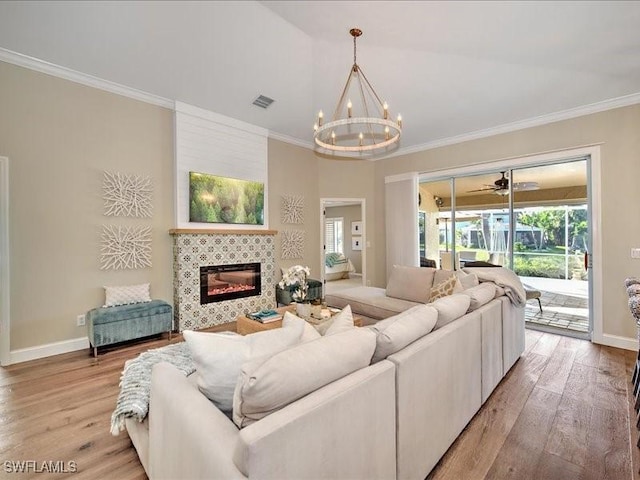 living room with ceiling fan with notable chandelier, light hardwood / wood-style floors, crown molding, and a tiled fireplace