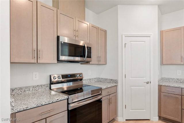 kitchen featuring light brown cabinets, light stone counters, and stainless steel appliances