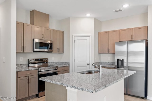 kitchen featuring light wood-type flooring, light stone counters, stainless steel appliances, a kitchen island with sink, and sink