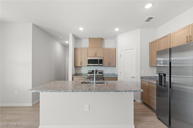 kitchen featuring light wood-type flooring, light stone counters, stainless steel appliances, a kitchen island with sink, and sink