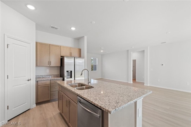 kitchen featuring a center island with sink, sink, light hardwood / wood-style flooring, light stone countertops, and appliances with stainless steel finishes