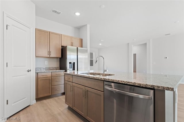 kitchen featuring light stone countertops, sink, stainless steel appliances, a kitchen island with sink, and light wood-type flooring