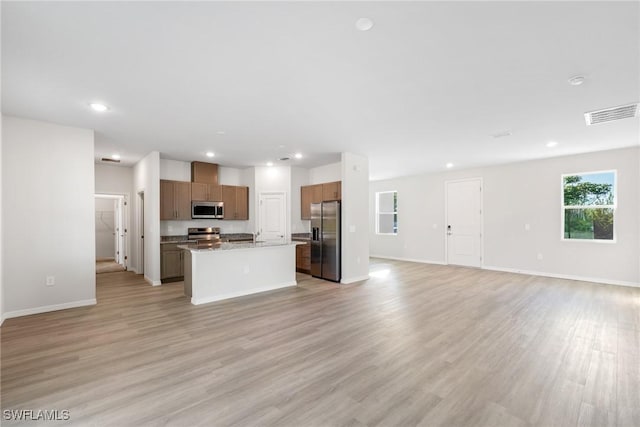 kitchen with light hardwood / wood-style floors, light stone countertops, stainless steel appliances, and a kitchen island with sink