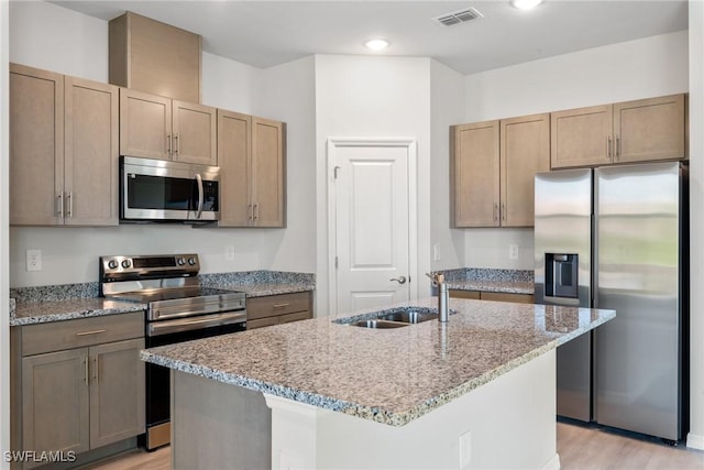 kitchen featuring a kitchen island with sink, sink, light hardwood / wood-style flooring, light stone counters, and stainless steel appliances