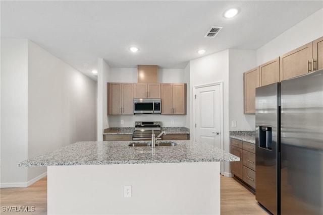 kitchen featuring light stone counters, light hardwood / wood-style flooring, an island with sink, and appliances with stainless steel finishes