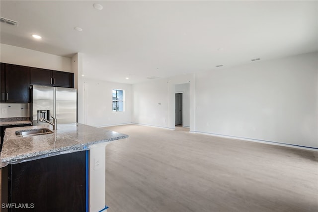 kitchen featuring stainless steel fridge, light stone counters, sink, light hardwood / wood-style flooring, and an island with sink