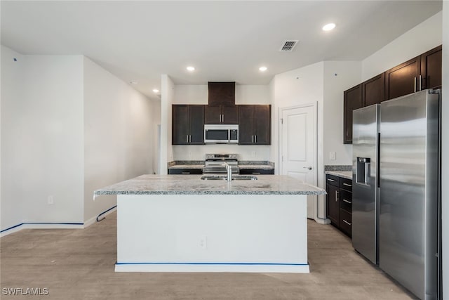 kitchen featuring dark brown cabinetry, sink, a kitchen island with sink, appliances with stainless steel finishes, and light wood-type flooring