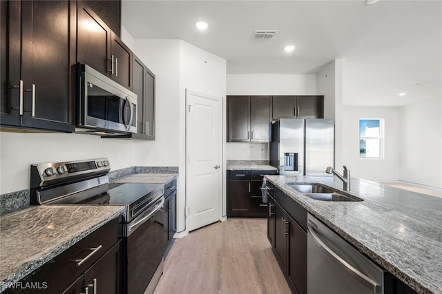 kitchen with appliances with stainless steel finishes, light stone counters, dark brown cabinets, and sink