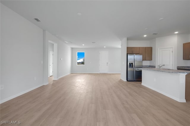 kitchen featuring light stone counters, light hardwood / wood-style flooring, a center island, and stainless steel refrigerator with ice dispenser