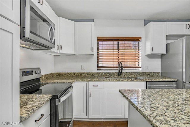 kitchen featuring stone countertops, appliances with stainless steel finishes, white cabinets, and a sink