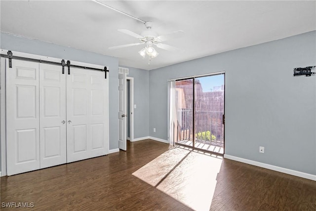 unfurnished bedroom featuring access to outside, a barn door, wood finished floors, and baseboards