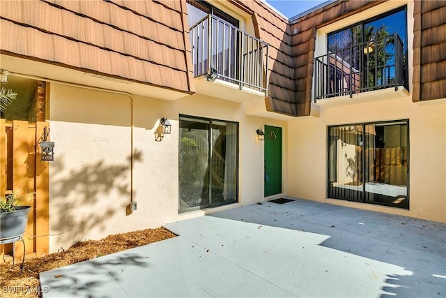 rear view of house featuring mansard roof, a patio area, a tile roof, and stucco siding