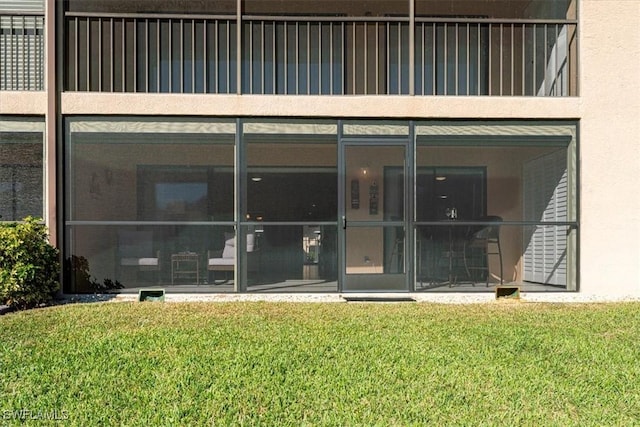 doorway to property featuring stucco siding, a lawn, and a balcony