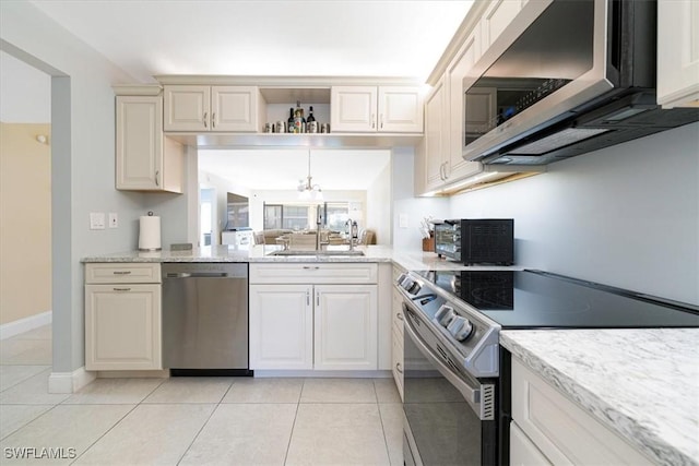 kitchen with a sink, light stone countertops, light tile patterned floors, and appliances with stainless steel finishes