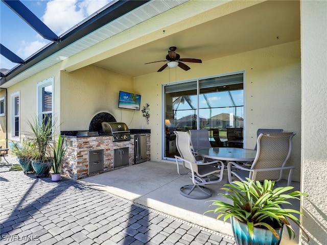 view of patio with an outdoor kitchen, ceiling fan, area for grilling, and glass enclosure