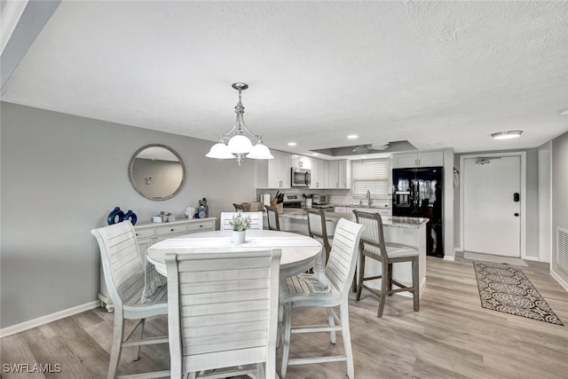 dining space with a textured ceiling, light wood-type flooring, a notable chandelier, and sink