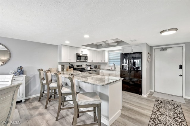 kitchen featuring light stone countertops, kitchen peninsula, white cabinetry, and stainless steel appliances