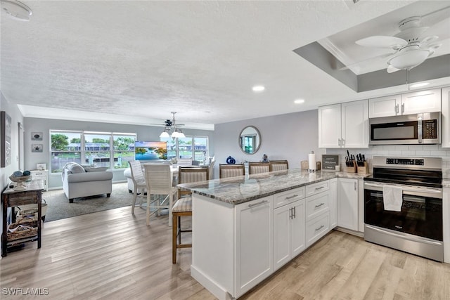 kitchen featuring white cabinetry, kitchen peninsula, a breakfast bar, appliances with stainless steel finishes, and light wood-type flooring