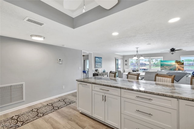 kitchen with ceiling fan with notable chandelier, light hardwood / wood-style floors, light stone countertops, and white cabinetry