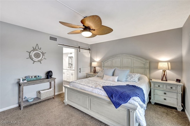 bedroom with a barn door, ceiling fan, ensuite bath, and light colored carpet