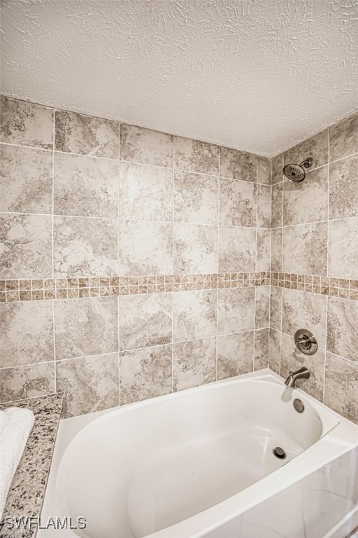 bathroom with a textured ceiling and tiled shower / bath combo