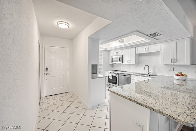 kitchen featuring light stone countertops, sink, kitchen peninsula, white cabinets, and appliances with stainless steel finishes