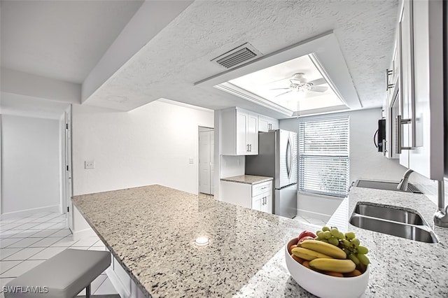 kitchen with white cabinets, sink, stainless steel fridge, light stone countertops, and a tray ceiling