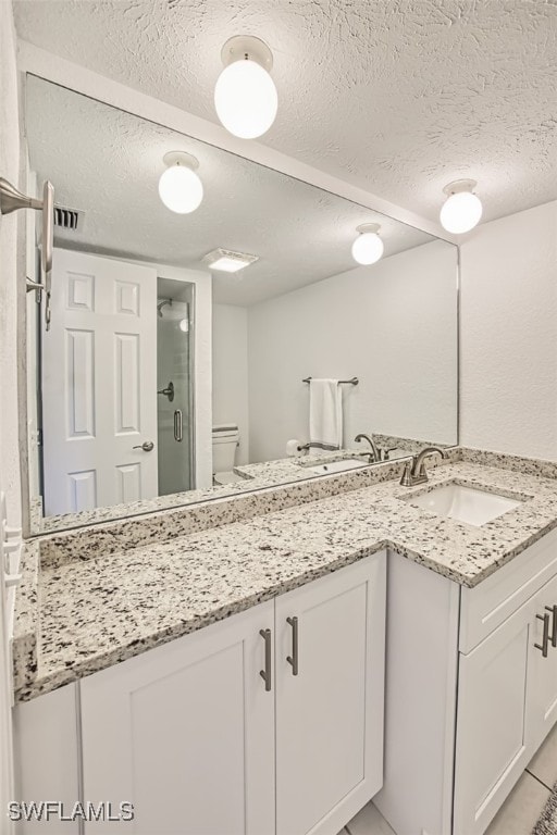 bathroom with vanity, a shower with shower door, a textured ceiling, and toilet