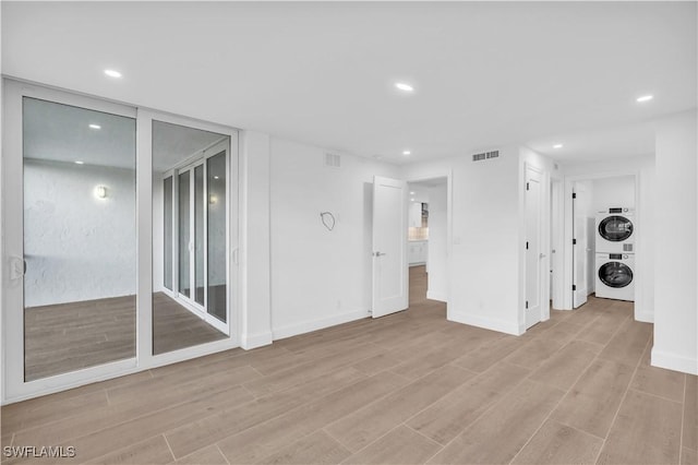 empty room with visible vents, light wood-style flooring, recessed lighting, stacked washer / dryer, and baseboards