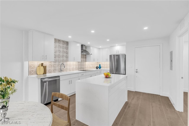 kitchen featuring light wood finished floors, stainless steel appliances, light countertops, wall chimney range hood, and tasteful backsplash