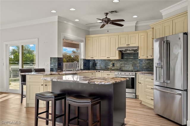 kitchen featuring appliances with stainless steel finishes, light stone counters, ornamental molding, a breakfast bar, and cream cabinetry