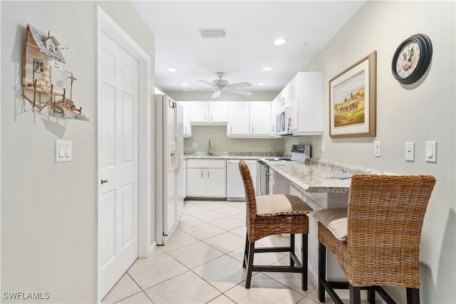 kitchen with kitchen peninsula, a kitchen bar, white appliances, sink, and white cabinetry