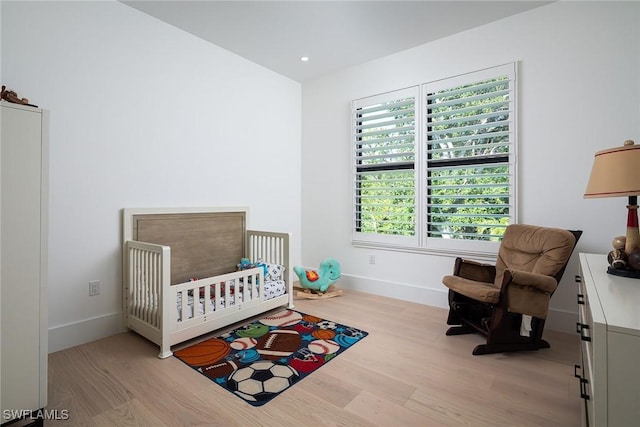 bedroom with light wood-type flooring and a nursery area