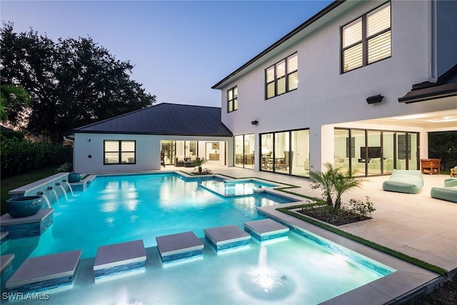 pool at dusk featuring an in ground hot tub and a patio