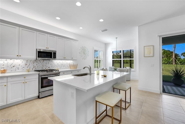 kitchen with an island with sink, sink, backsplash, a kitchen breakfast bar, and stainless steel appliances