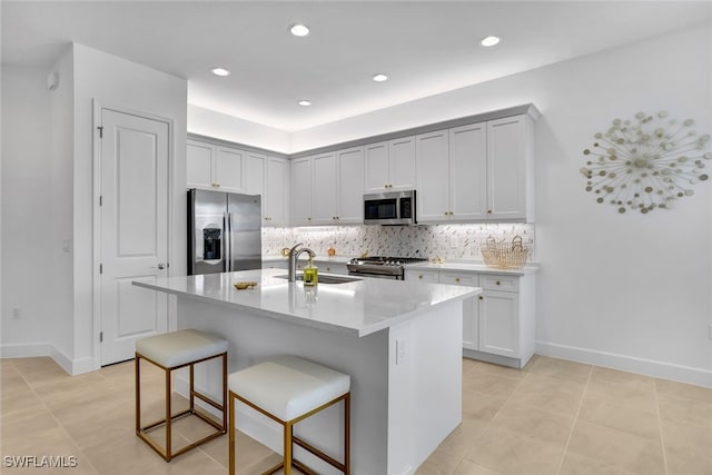 kitchen with appliances with stainless steel finishes, sink, a kitchen breakfast bar, decorative backsplash, and a kitchen island with sink