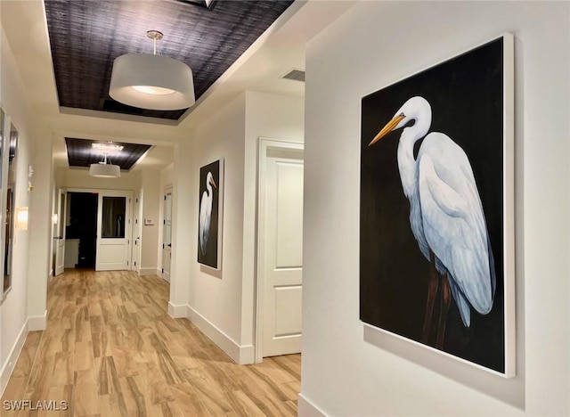 hallway with light hardwood / wood-style floors and a raised ceiling