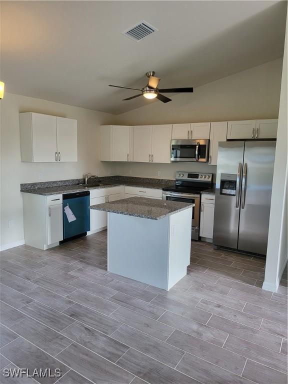 kitchen with a center island, dark stone counters, ceiling fan, appliances with stainless steel finishes, and white cabinetry