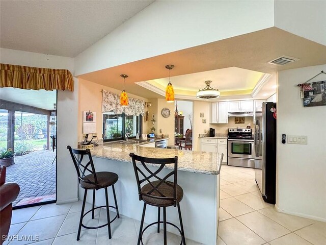 kitchen featuring white cabinetry, stainless steel appliances, kitchen peninsula, a tray ceiling, and a breakfast bar