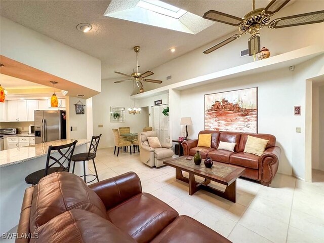 tiled living room with ceiling fan with notable chandelier, a textured ceiling, high vaulted ceiling, and a skylight